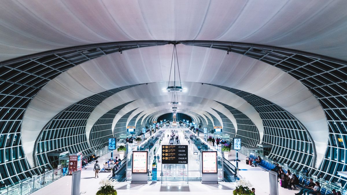 Suvarnabhumi Airport Bangkok terminal interior with glass roof and arriving passengers — main Bangkok airport for Singapore to Bangkok flights